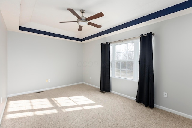 carpeted spare room with baseboards, a raised ceiling, visible vents, and a ceiling fan