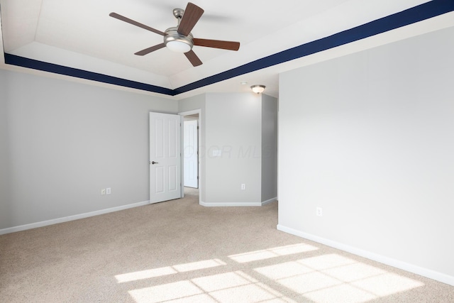 carpeted spare room with a raised ceiling, a ceiling fan, and baseboards