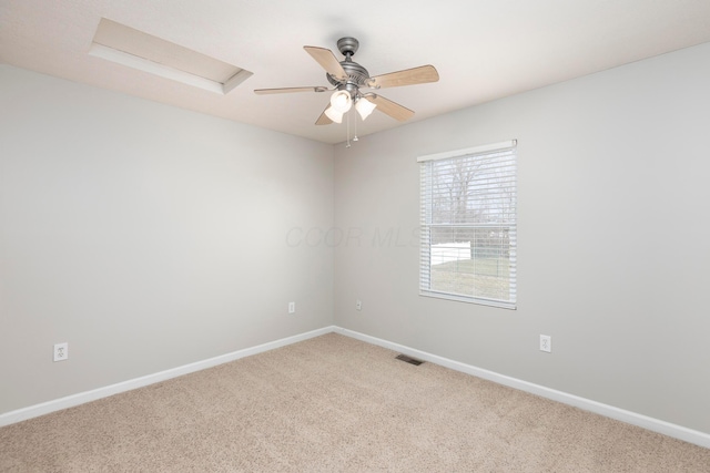 carpeted spare room featuring visible vents, baseboards, attic access, and a ceiling fan