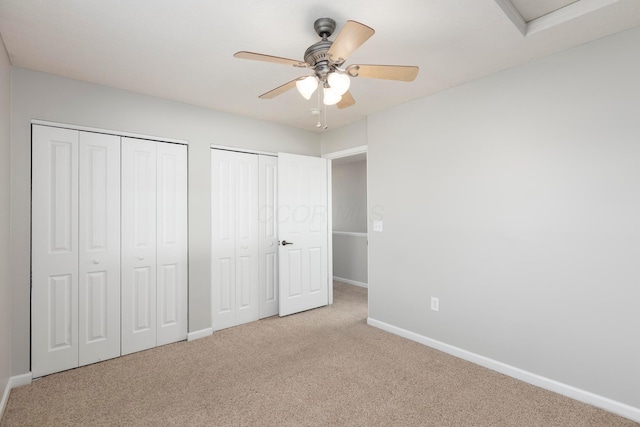 unfurnished bedroom with a ceiling fan, carpet flooring, baseboards, and multiple closets