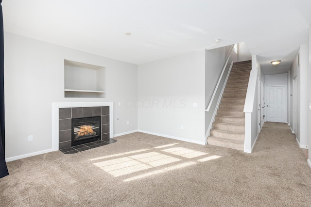 unfurnished living room featuring baseboards, stairway, built in features, carpet floors, and a tile fireplace