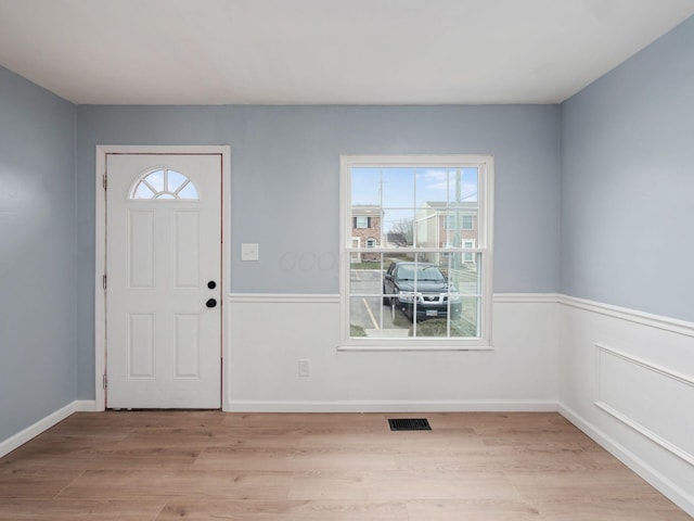 entrance foyer with light wood finished floors, wainscoting, visible vents, and baseboards