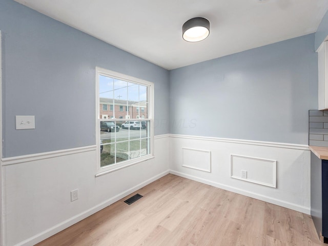 interior space featuring light wood-style flooring, visible vents, and wainscoting