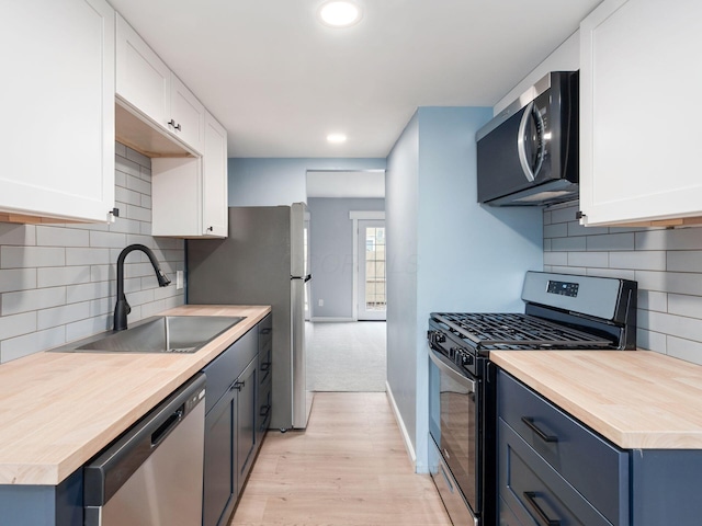 kitchen featuring appliances with stainless steel finishes, a sink, light wood-style floors, and white cabinets