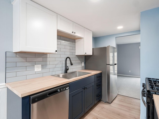 kitchen featuring appliances with stainless steel finishes, white cabinets, a sink, and light wood-style flooring