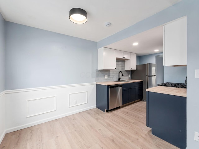 kitchen featuring light wood-style flooring, decorative backsplash, appliances with stainless steel finishes, white cabinets, and a sink