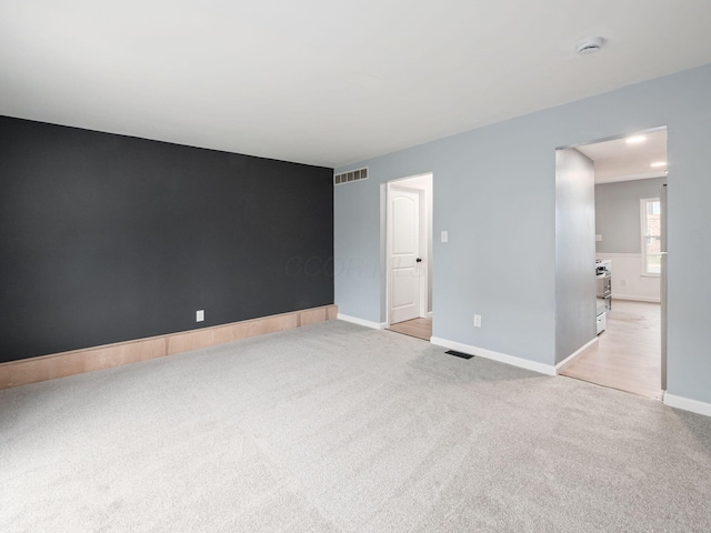 carpeted spare room with an accent wall, visible vents, and baseboards