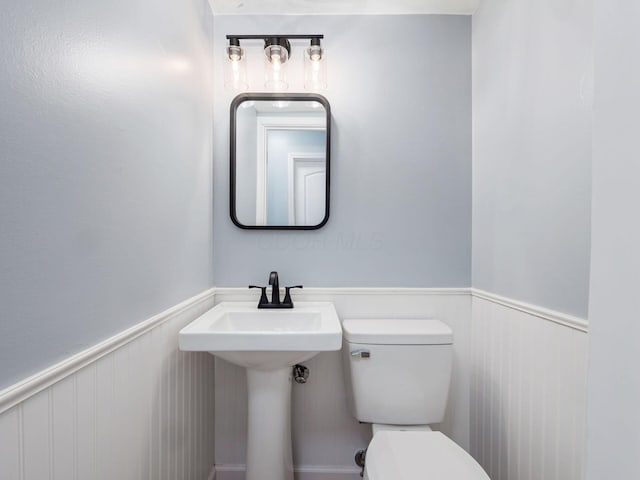 half bath featuring wainscoting and toilet