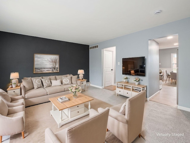 living area featuring baseboards, an accent wall, visible vents, and light colored carpet