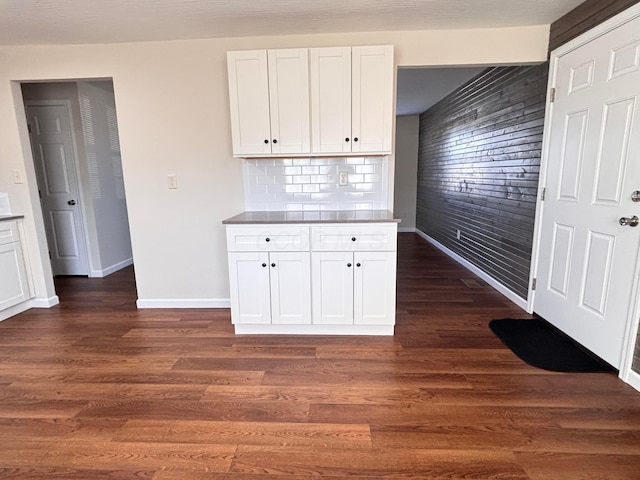 kitchen featuring wood walls, white cabinetry, baseboards, tasteful backsplash, and dark wood finished floors