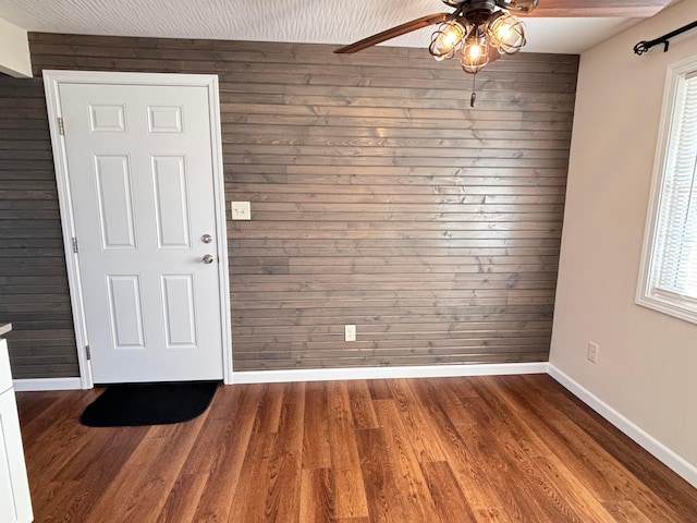 interior space with dark wood-style floors, wooden walls, baseboards, and a ceiling fan