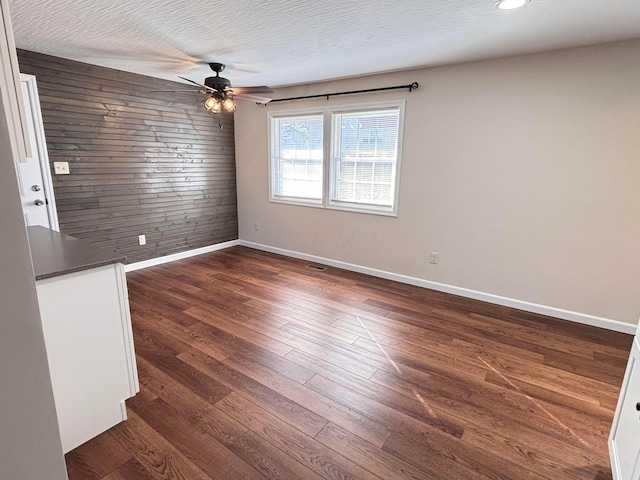 unfurnished room featuring dark wood-style floors, ceiling fan, baseboards, and wood walls