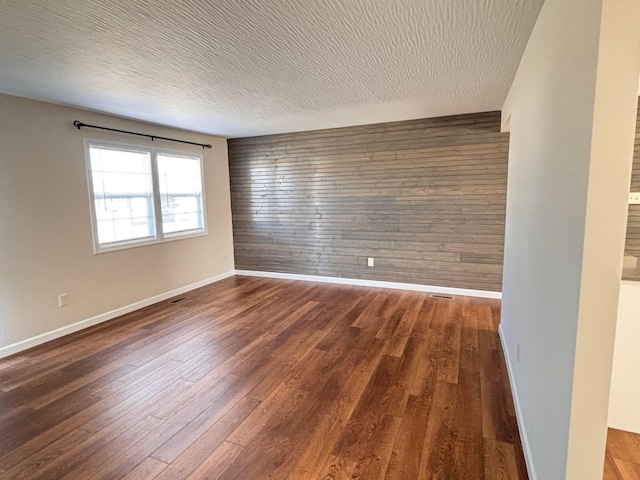 spare room featuring wooden walls, a textured ceiling, baseboards, and wood finished floors