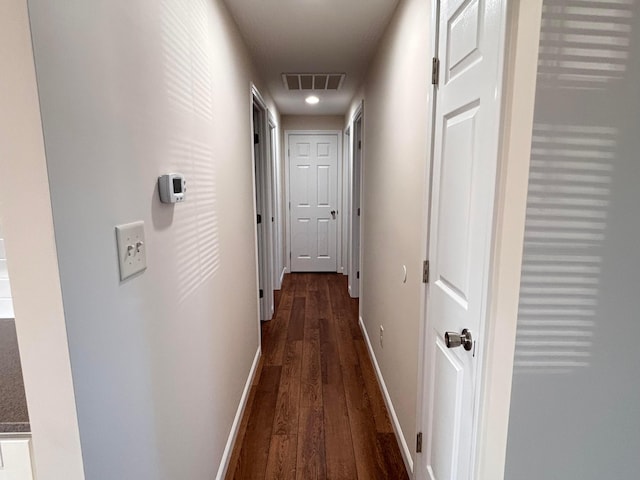 hall featuring dark wood-type flooring, visible vents, and baseboards