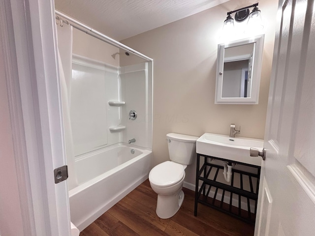 bathroom with shower / washtub combination, toilet, a sink, wood finished floors, and baseboards