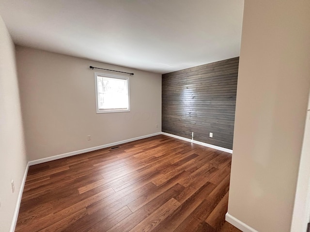 empty room featuring an accent wall, dark wood finished floors, wood walls, and baseboards