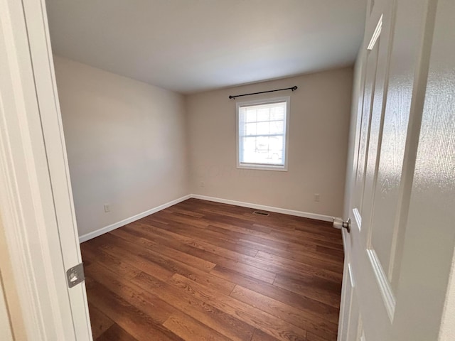 empty room with visible vents, dark wood finished floors, and baseboards