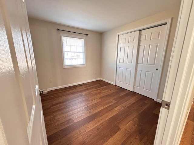 unfurnished bedroom featuring a closet, visible vents, dark wood finished floors, and baseboards