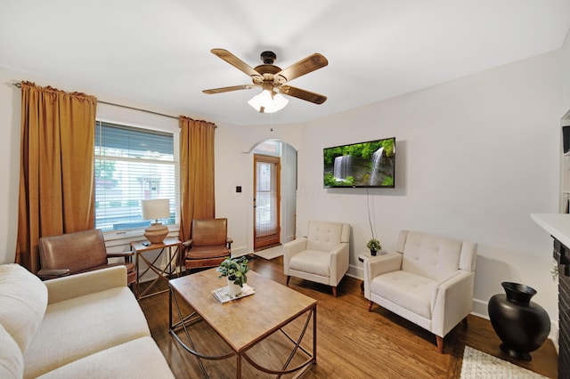 living area featuring a ceiling fan, arched walkways, baseboards, and wood finished floors