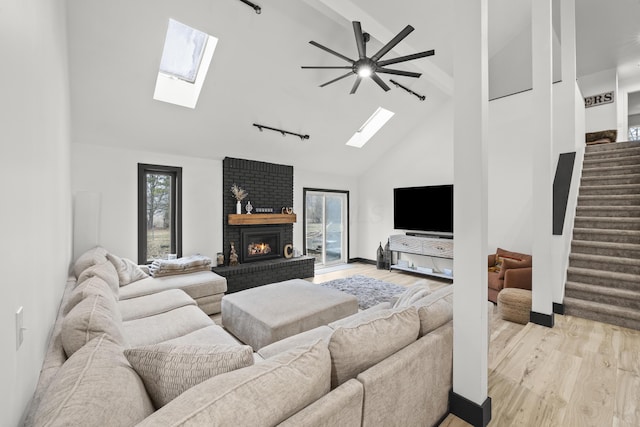 living room featuring stairs, a brick fireplace, light wood finished floors, and high vaulted ceiling