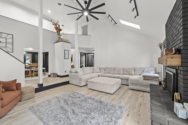 living room with track lighting, a fireplace, a skylight, wood finished floors, and high vaulted ceiling