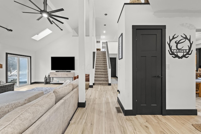 living room featuring baseboards, stairway, light wood-type flooring, a skylight, and high vaulted ceiling