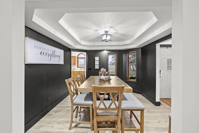 dining space with light wood-type flooring, a raised ceiling, and baseboards