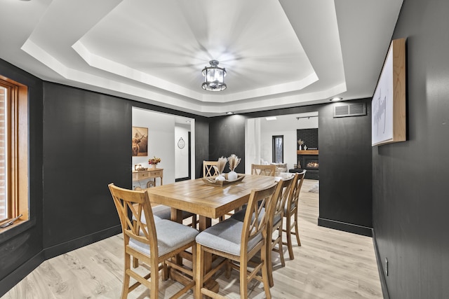 dining area featuring a tray ceiling, baseboards, light wood-style floors, and visible vents