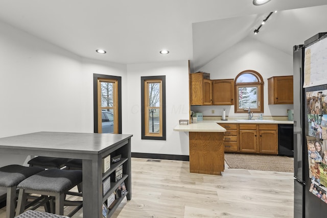 kitchen featuring light wood finished floors, dishwasher, a peninsula, brown cabinetry, and a sink