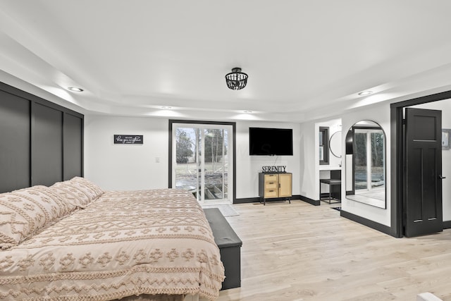 bedroom with baseboards, a tray ceiling, light wood-style floors, and access to outside