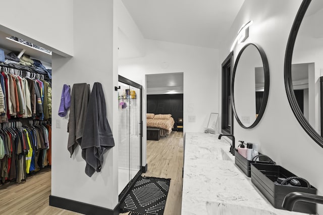 ensuite bathroom featuring a spacious closet, connected bathroom, vaulted ceiling, wood finished floors, and a sink