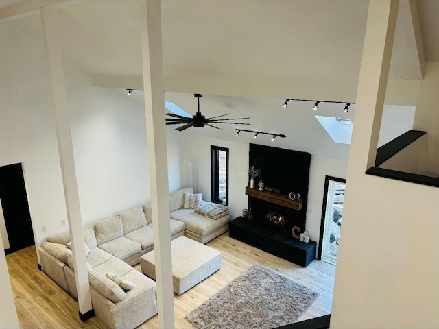 living room featuring a skylight, a warm lit fireplace, wood finished floors, and a ceiling fan