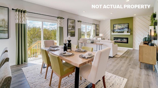 dining area with a glass covered fireplace, wooden walls, recessed lighting, and light wood finished floors