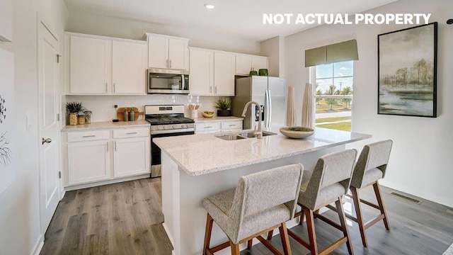 kitchen with a sink, stainless steel appliances, decorative backsplash, and light wood finished floors