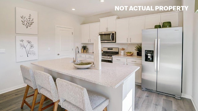 kitchen featuring wood finished floors, a center island with sink, a sink, stainless steel appliances, and white cabinetry