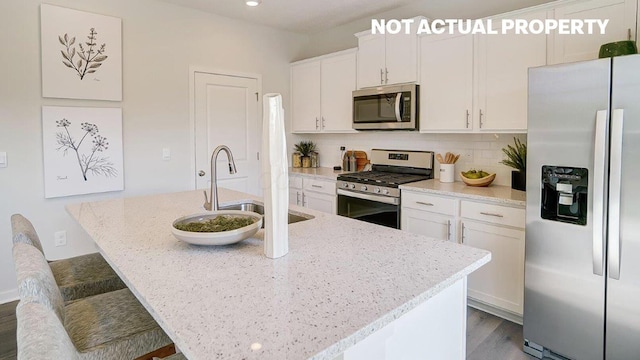 kitchen featuring an island with sink, light stone counters, backsplash, white cabinetry, and stainless steel appliances