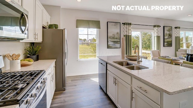 kitchen with a sink, backsplash, wood finished floors, white cabinetry, and stainless steel appliances