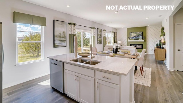 kitchen featuring a kitchen island with sink, wood finished floors, dishwasher, and a glass covered fireplace