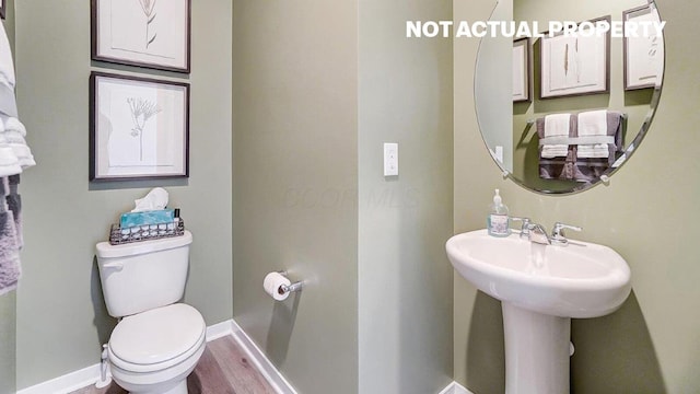 half bathroom with baseboards, toilet, and wood finished floors