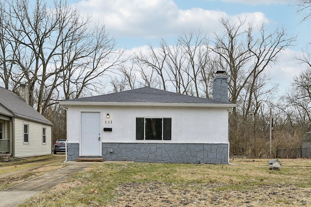 bungalow-style house featuring roof with shingles, a chimney, a front lawn, and stucco siding