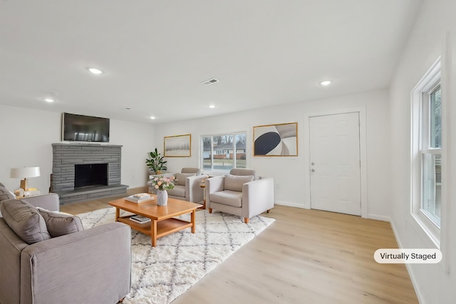 living room featuring a stone fireplace, recessed lighting, visible vents, baseboards, and light wood-style floors