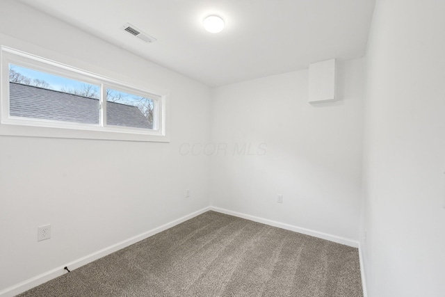 spare room with dark colored carpet, visible vents, and baseboards