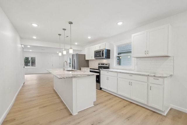 kitchen featuring stainless steel appliances, white cabinetry, backsplash, light wood finished floors, and an island with sink