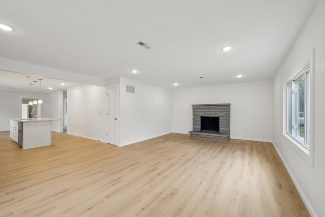 unfurnished living room featuring light wood-type flooring, visible vents, a fireplace with raised hearth, and recessed lighting