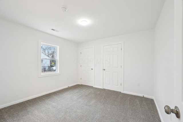 unfurnished bedroom featuring dark colored carpet, visible vents, and baseboards