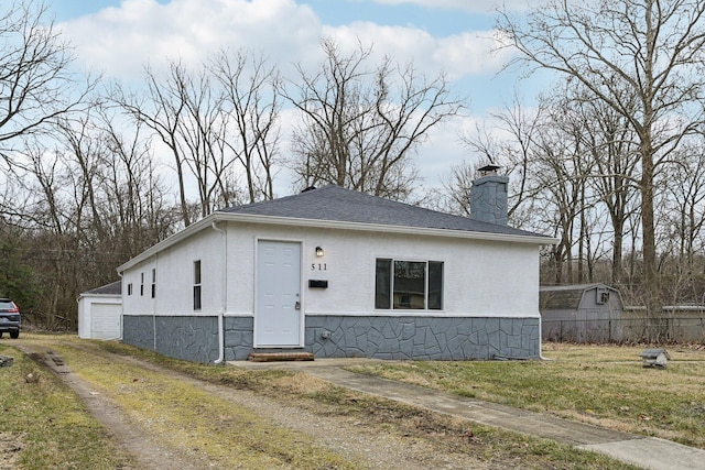 bungalow-style home featuring an outbuilding, a chimney, stucco siding, stone siding, and a front lawn