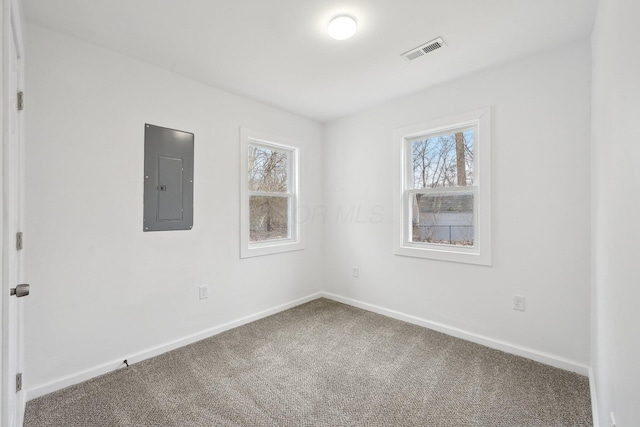 carpeted spare room featuring baseboards, electric panel, visible vents, and a wealth of natural light