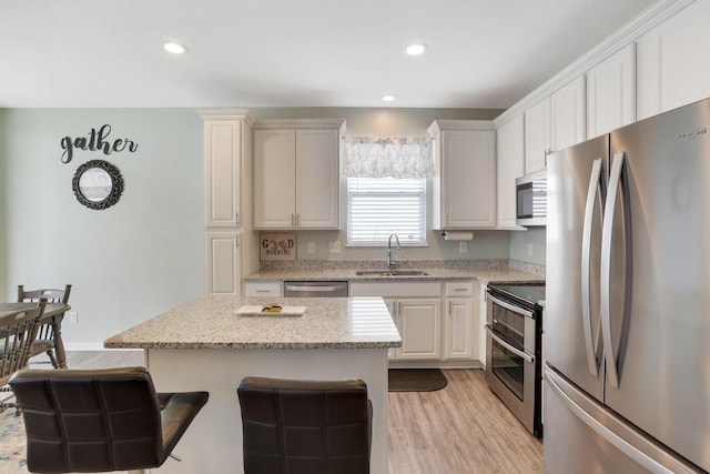 kitchen with a center island, light stone counters, appliances with stainless steel finishes, light wood-style floors, and a sink