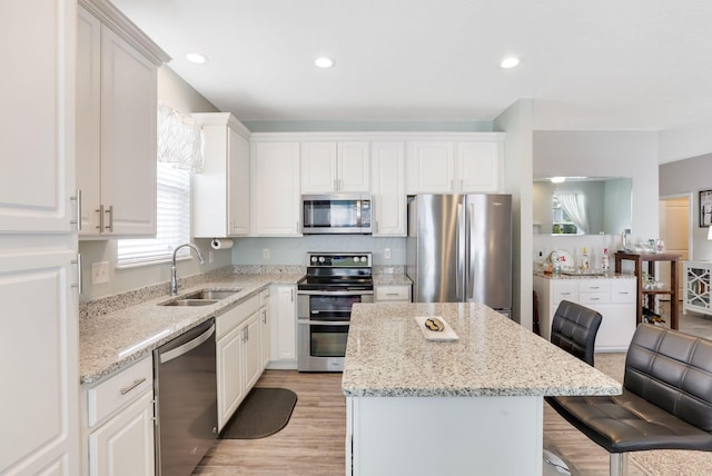 kitchen with a sink, a center island, appliances with stainless steel finishes, a breakfast bar area, and light stone countertops