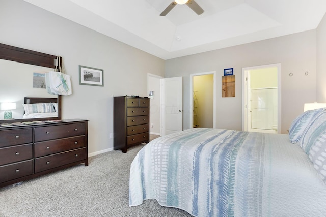 bedroom featuring a ceiling fan, a tray ceiling, connected bathroom, baseboards, and light colored carpet